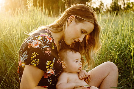 woman carrying baby sitting on grass field thumbnail