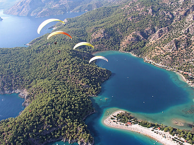 aerial view of four parachutes over body of waters and mountains thumbnail