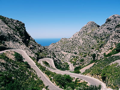 zigzag road beside cliff near sea under blue sky thumbnail