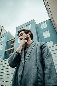 man in gray coat while holding his chin thumbnail