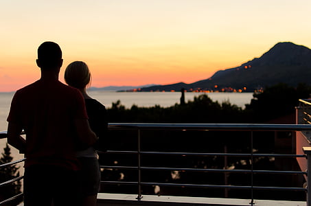 silhouette photography of couple standing on terrace facing mountain thumbnail