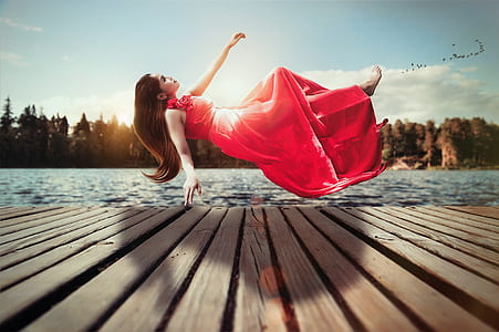 woman in red sleeveless dress floating above brown wooden dock during daytime thumbnail