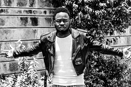 Man Wearing Leather Jacket Standing Near Concrete Wall Beside Plants thumbnail