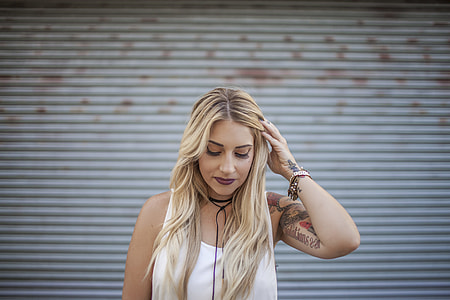 woman standing wearing white tank-top holding her hair thumbnail