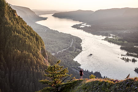 landscape photo of person on top of hill near body of water thumbnail