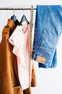 blue jeans and brown coat hanging on black bar thumbnail