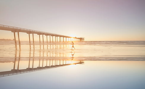 person walking on shallow water near bridge during golden hour thumbnail