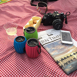 Nikon DSLR camera beside three assorted-color carabiner speaker and newspaper thumbnail
