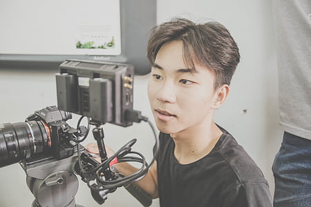 man watching on screen while holding camera beside person standing beside wall thumbnail