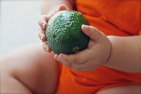 toddler holding a round green fruit thumbnail