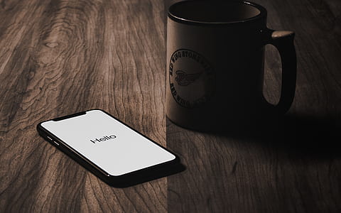 turned on iPhone X beside brown ceramic mug on brown surface thumbnail