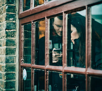 man holding iPhone beside woman standing near brown wooden framed clear glass window thumbnail