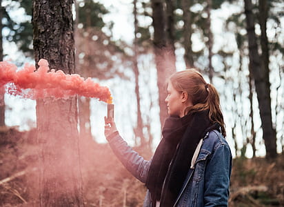 woman standing beside tree holding pink smoke thumbnail