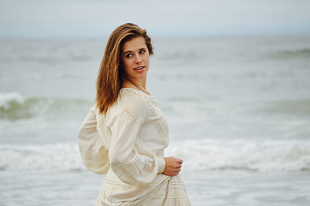 woman looking at back while walking on beach shore thumbnail