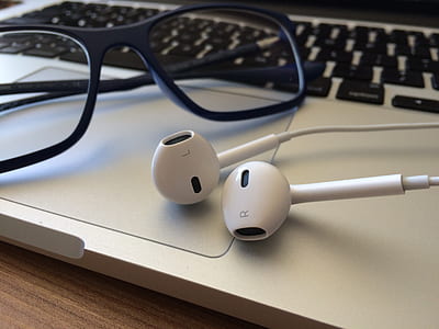 Apple EarPods beside black framed eyeglasses on top of MacBook Air thumbnail