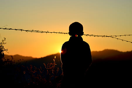 Silhouette of Boy Standing Near Barbed Wire Fence during Golden Hour thumbnail