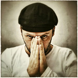 photo of man wearing black cap and white shirt covering his nose thumbnail