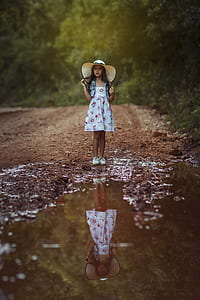 girl holding hair standing on dirt near road surrounded by trees during daytime thumbnail