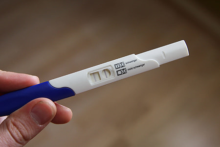 person holding white and blue disposable pregnancy test displaying positive thumbnail