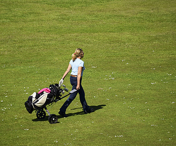 woman walking while holding golf trolley with golf set on grass field at daytime thumbnail