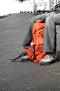 selective-color photography of orange backpack between person's leg sitting thumbnail