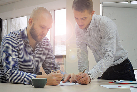 two men writing on white paper inside white painted room thumbnail