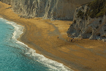 people on seashore beside gray rock hill aerial photo thumbnail