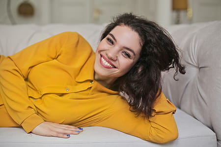 A young woman wearing yellow button-up shirt top smiling while lying down on the couch with her hand on the back of her head thumbnail