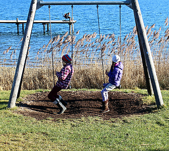 two girls sitting on playground swing thumbnail