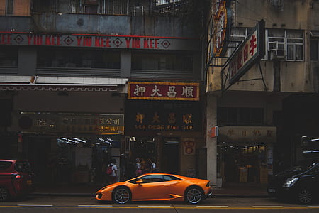 orange Lamborghini coupe parking near beside gray concrete building thumbnail