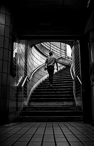 grayscale photo of man carrying books while walking on stairs at a subway station thumbnail