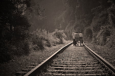 grayscale photo of three persons walking on railway thumbnail