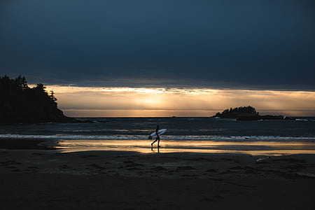 person holding white surfboard walking on seashore thumbnail