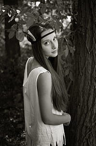 grayscale photo of woman standing beside tree thumbnail