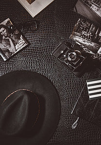 greyscale photo of black fedora hat beside black camera and black framed eyeglasses thumbnail