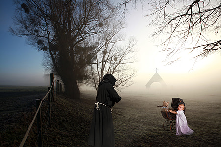 toddler standing beside stroller in front of person in hooded robe near fence outdoor thumbnail