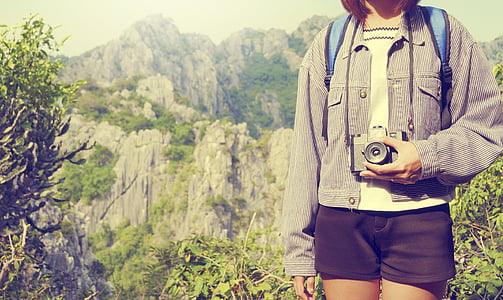 woman holding camera near mountain thumbnail