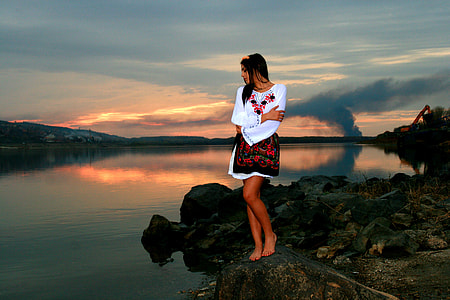 woman in white and red dress standing on rock cliff near body of water during sunset thumbnail