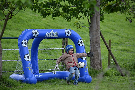 smiling boy playing football beside goal net during daytime thumbnail