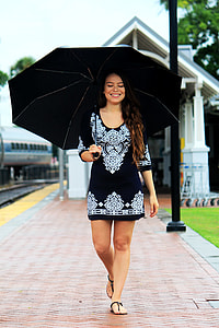 woman in black and white tribal elbow-sleeved scoop-neck minidress with black umbrella walking on brown pathway during daytime thumbnail
