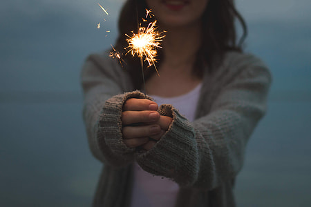 shallow focus photography of woman in gray knitted cardigan holding fireworks thumbnail