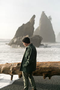 man standing on seashore beside driftwood thumbnail