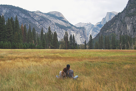 two person sitting on grass field facing alps across the forest during daytime thumbnail