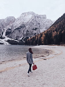 woman holding red tote bag while walking on the path of sand near body of water thumbnail