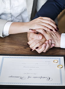 two person holding hands near certificate with two gold-colored rings thumbnail