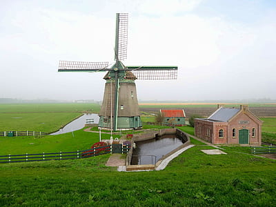 windmill with lake and house on farmland at daytime thumbnail