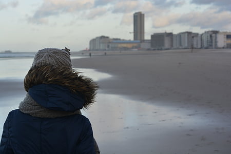 person wearing black and brown hoodie standing on gray beach shore during daytime thumbnail