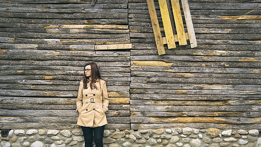woman in beige coat leaning on brown wall thumbnail