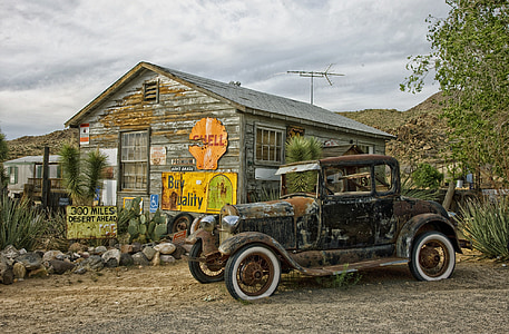 rusted vintage black and brown vehicle near brown and white wooden house under cloudy blue sky at daytime thumbnail