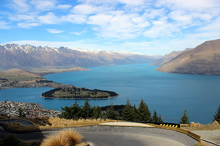 trees near body of water and mountains under cloudy sky thumbnail